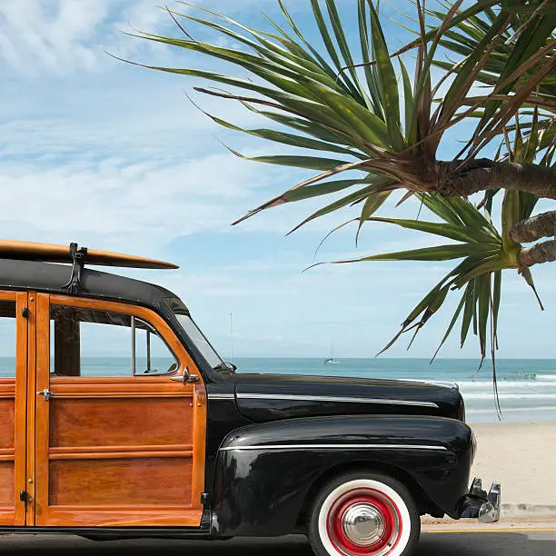 vintage woodie car with surfboard on the roof parkedwith beach background
