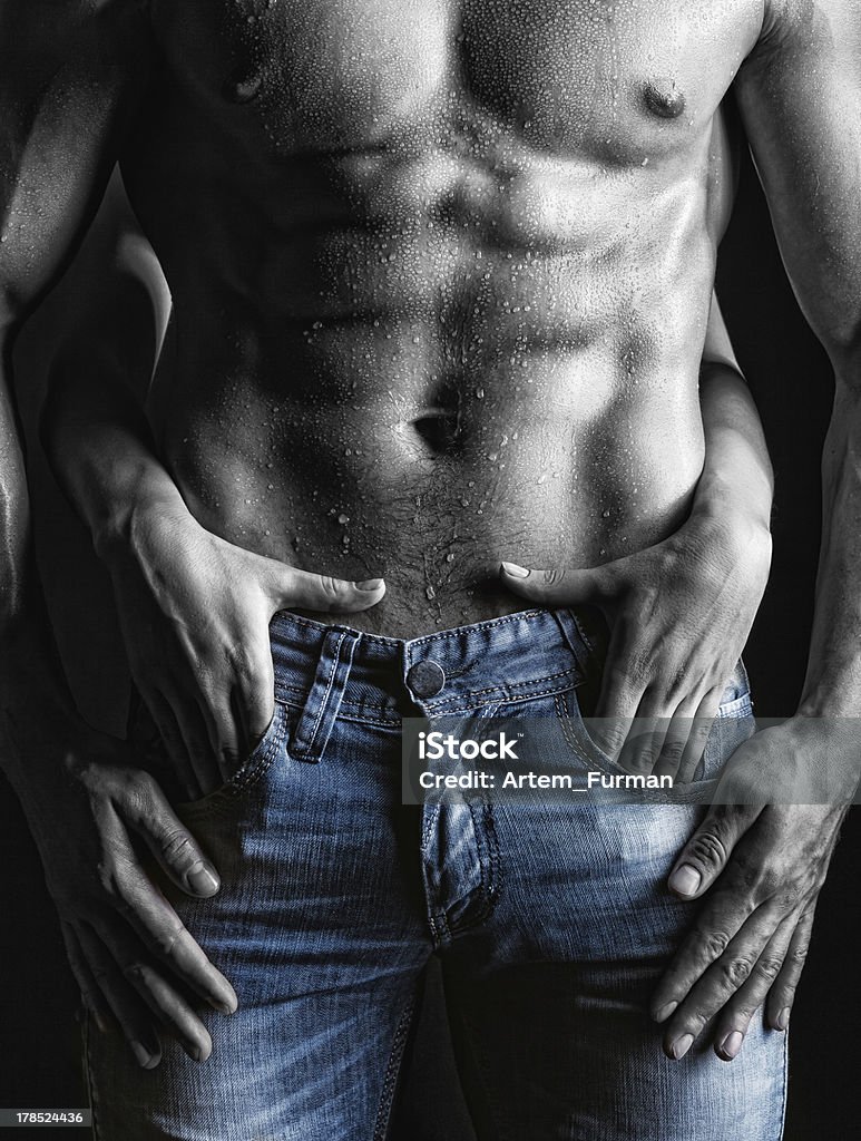 Sexy guy Sexy muscular naked man and female hands unbuckle his jeans on a dark background Sensuality Stock Photo