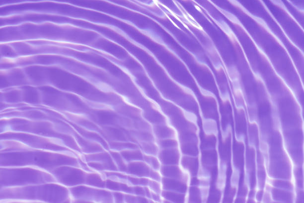 Purple water bubbles with ripples on the surface. Transparent pink colored clear calm water surface texture with splashes and bubbles. Water waves with shining pattern texture background.