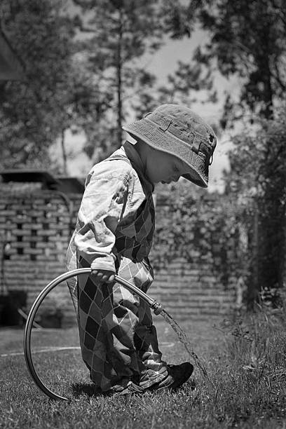 Little boy with hat watering grass stock photo
