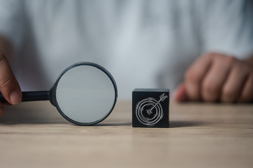 Target board icon in wood block and man use magnifier glass for focus business objective achievement. The concept of search, goal, strategy and success.