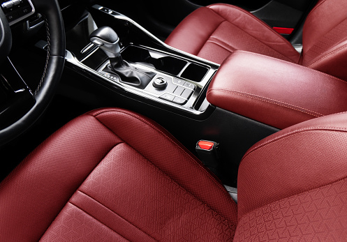 Modern car Interior. Steering wheel, shift lever and dashboard. Detail of modern car interior. Automatic gear stick. Part of red leather seats with stitching in expensive car