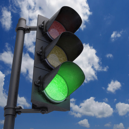 Traffic Light in a blue sky with only the green light on.
