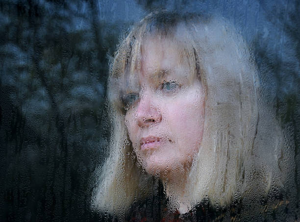 Blurred portrait of the middle-aged woman looking through the window on a rainy day