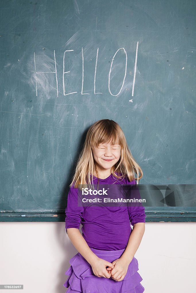 Smiling girl with word hello on chalkboard Studio portrait of smiling young girl with eyes closed in classroom with word hello written on chalkboard Chalk - Art Equipment Stock Photo