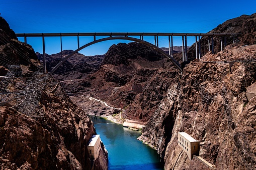 A suspension bridge is seen crossing over a deep canyon, leading to a tranquil blue river below