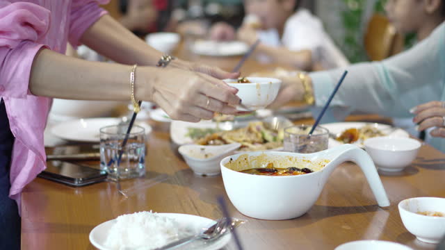 Portrait Asian woman scoops tom yam shrimp in a white bowl and serves it to the family on the table.