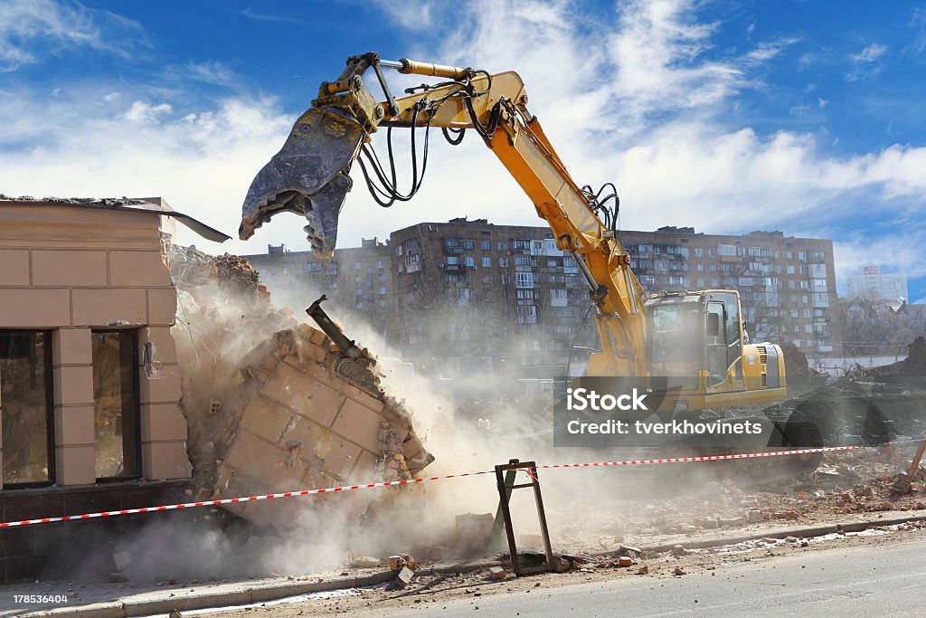 Building demolition machine pulls down a wall on a sunny day Bulldozer crushing the building at construction site Demolishing Stock Photo