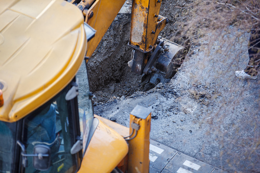 Excavator excavator digging a hole, breaking street asphalt. Excavator and  worker repairing damaged water supply pipe