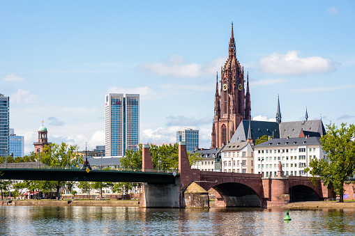 Frankfurt am Main, Germany - August 17, 2023: The bell tower of Frankfurt Cathedral (Imperial Cathedral of Saint Bartholomew) overlooks the Alte Brücke, the old stone bridge over the river Main.