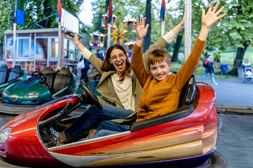 Shared laughter and playful collisions strengthen the bond between a parent and their child as they navigate bumper cars, experiencing pure joy and togetherness at the amusement park