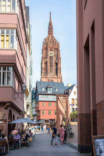 Frankfurt am Main, Germany - August 17, 2023: The bell tower of Frankfurt Cathedral overlooks the medieval townhouses and narrow streets of the Altstadt with sidewalk cafes frequented by tourists.
