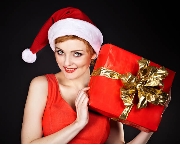 woman wearing santa hat  holding  Christmas gift stock photo