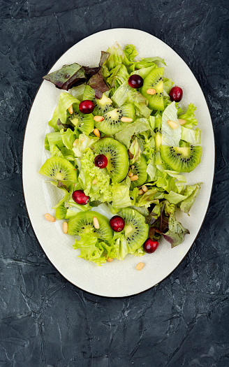 Delicious fresh salad of kiwi, leafy greens, berries and pine nuts. Top view.