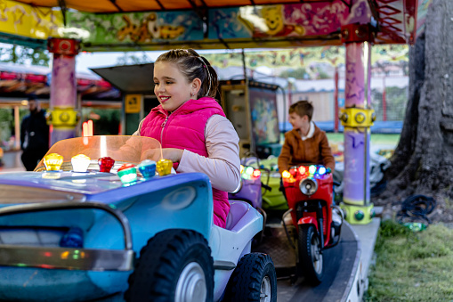 With a sense of wonder, a child hops on a motorized vehicle and embarks on a whimsical adventure, spinning round and round, creating magical moments at the amusement park
