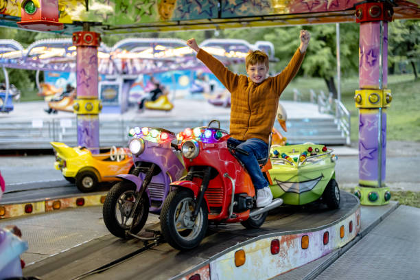 kind findet nervenkitzel und lächeln auf motorisiertem kreisverkehr im vergnügungspark - the thrills stock-fotos und bilder