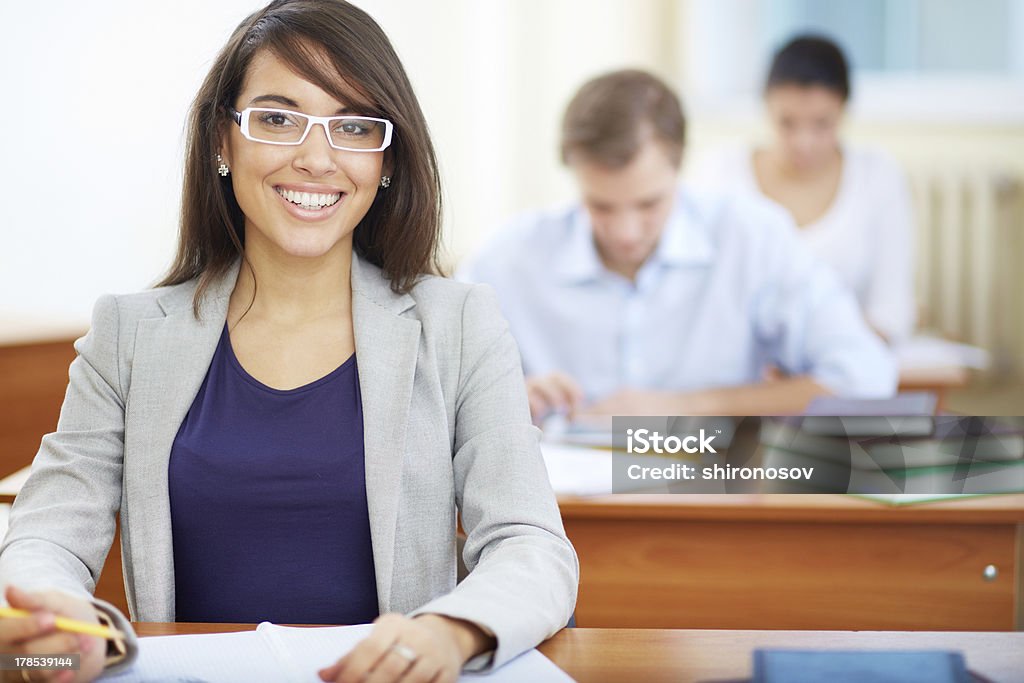 Pretty student Portrait of female student looking at camera at lesson on background of two group mates Adult Stock Photo