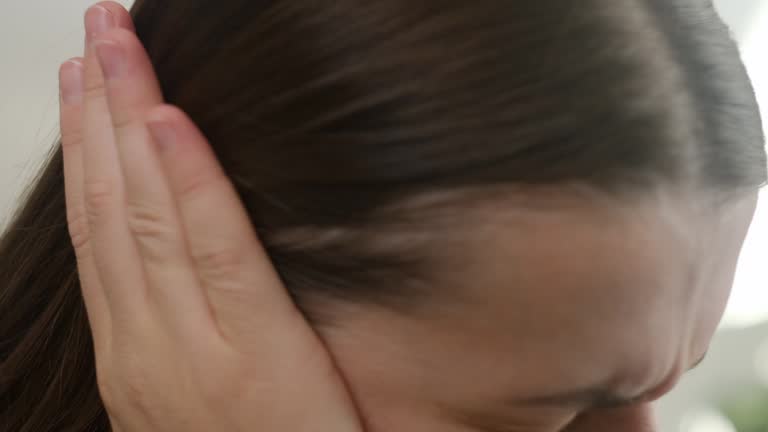 Closeup up side profile of sick sad young caucasian female having ear pain touching painful head sitting on sofa. Unhealthy tired woman suffering from painful otitis. Health care and tinnitus concept