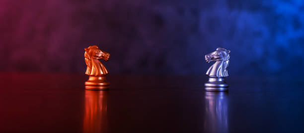 Chess pieces knights facing each other for a standoff. Chess knights confronting each other. Chess knights head to head. Chess horses face each other in warm and cold tones.