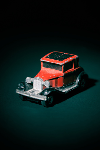 Old red toy car against dark green background