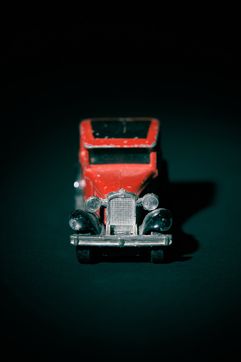 Old red toy car against dark green background