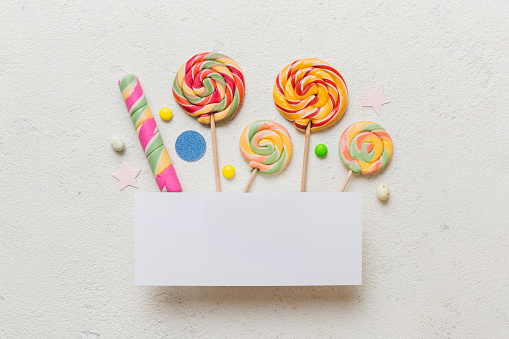 Flat lay holiday composition. Paper blank, lollipop, birthday decorations on Colored background. Top view, copy space for text.