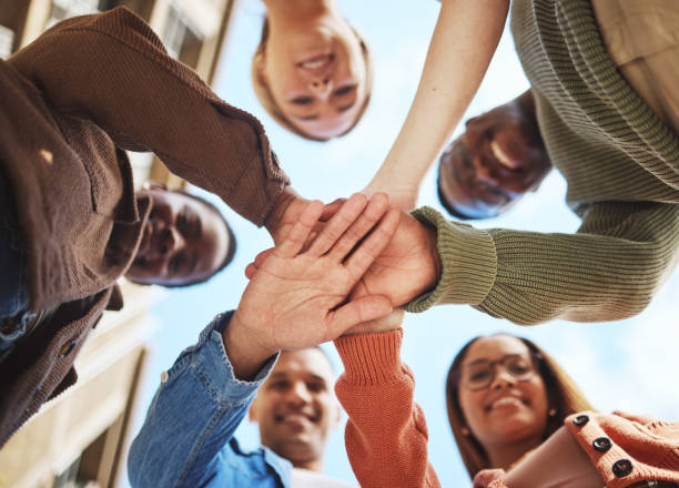 istock Friends smile, hands together in huddle and group diversity, team building in circle from below. Friendship, happiness and support, university students smiling, happy men and women on college campus. 1785432284