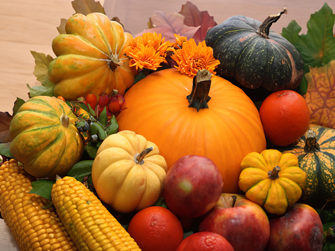 Pumpkins, gourds, corn, apples, flowers, and leaves sit on a wooden surface.