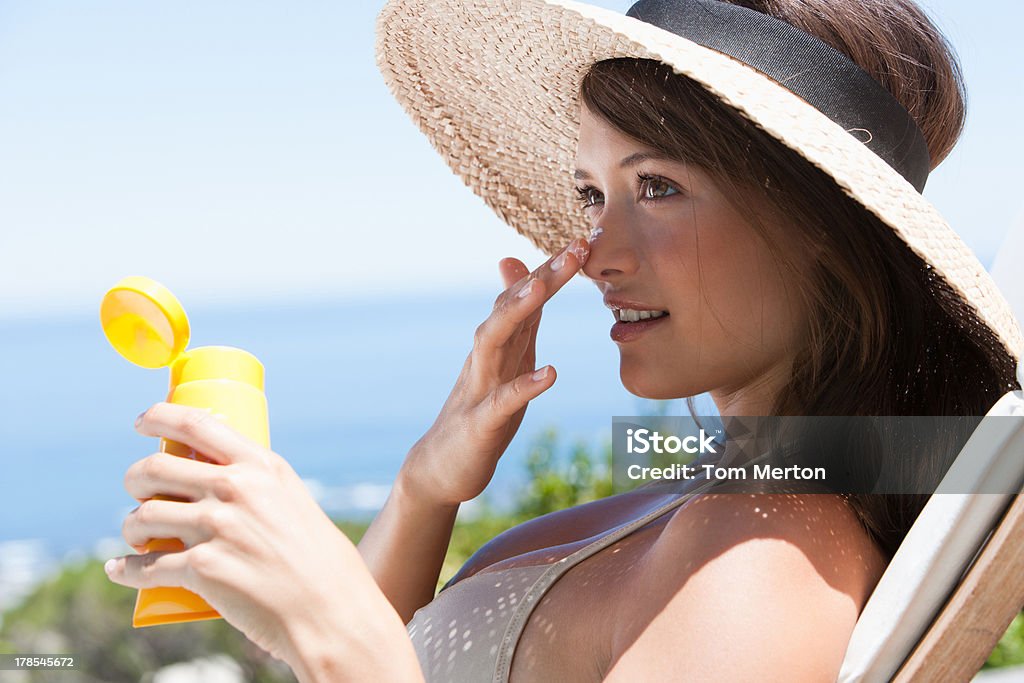 Mulher com chapéu de palha aplicar protetor solar para face ao ar livre - Foto de stock de Protetor Solar royalty-free