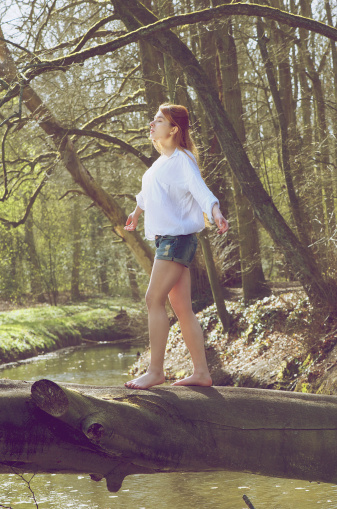 Portrait of a young woman balancing on fallen tree trunk across a stream
