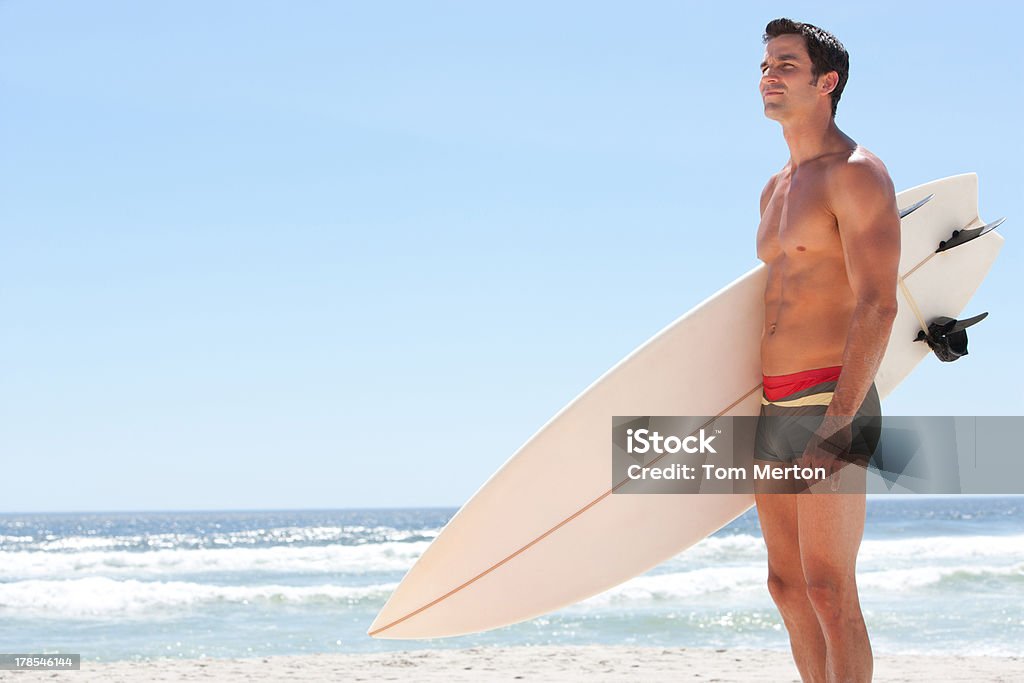 Hombre con tabla de surf en la playa - Foto de stock de Bañador de hombre libre de derechos