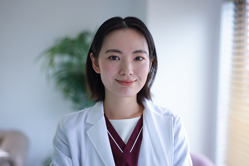 Young Asian Female Doctor Looking At Camera in front of office background