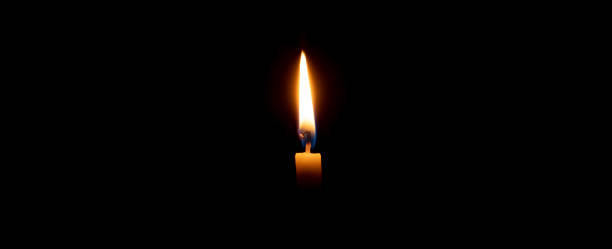 istock A single burning candle flame or light glowing on an orange candle on black or dark background on table in church for Christmas, funeral or memorial service with copy space 1785513685