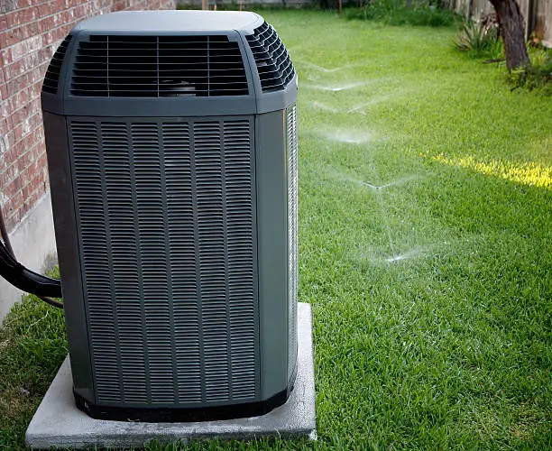 Modern high efficiency air conditioner on backyard with working sprinkler system