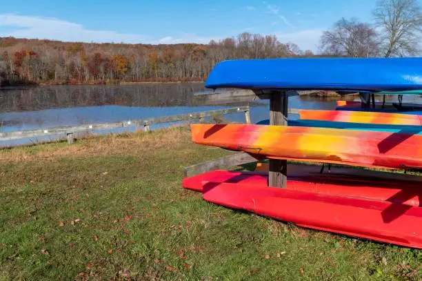 Photo of Racks of colorful kayaks and canoes in green grass by majestic autumn fishing lake fall colors background