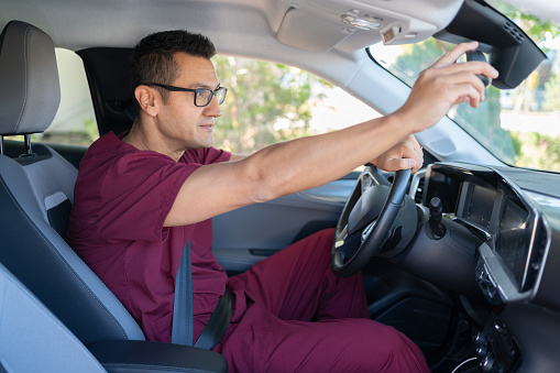 Man In Medical Scrubs Adjusting The Rearview Mirror In Car
