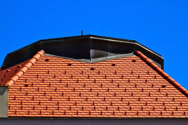 stucco finished building with attractive roof. sloped Zink tile Zink rooftop. metal snow guard brackets in geometric pattern. tin gutter and downspout. modern architecture. blue sky