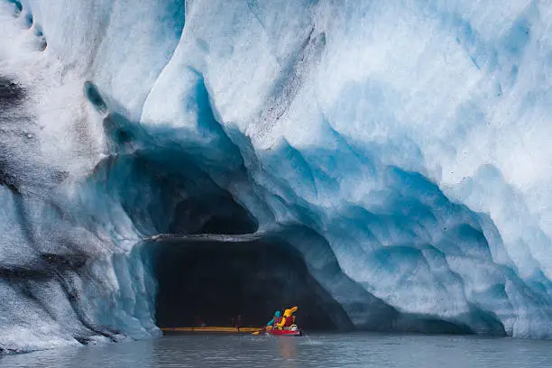 Kayaking into blue ice cave in glacier iceberg, Alaska
