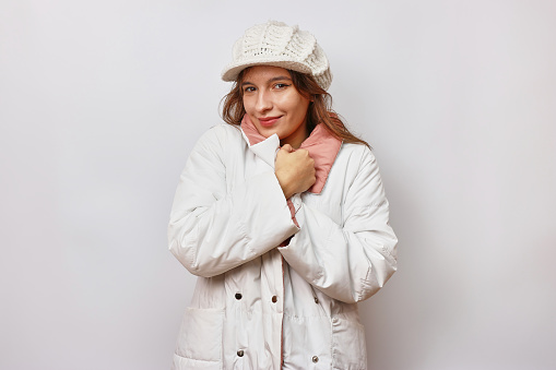 A beautiful girl is dressed in a white autumn raincoat and a white warm hat.