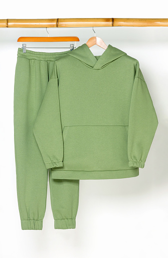 A green sports hoodie and pants hang on a wooden bamboo hanger.The concept of sport, convenience and unisex.