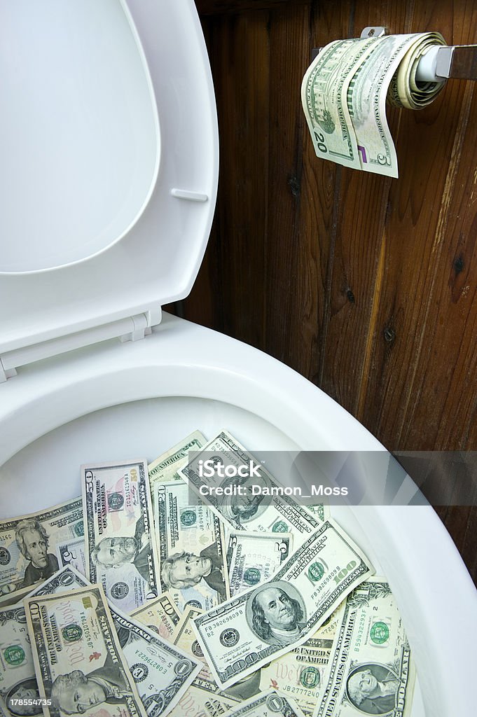 Flushing Money in the Toilet Toilet bowl full of cash with a roll of toilet paper made of money hanging beside it Flushing Toilet Stock Photo