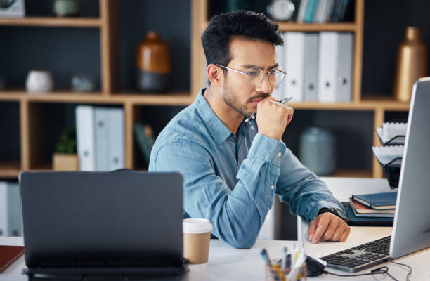 istock Serious asian man, thinking and computer for digital marketing, project planning or schedule at office desk. Male creative designer in thought working on PC and laptop for market or startup strategy 1785551836
