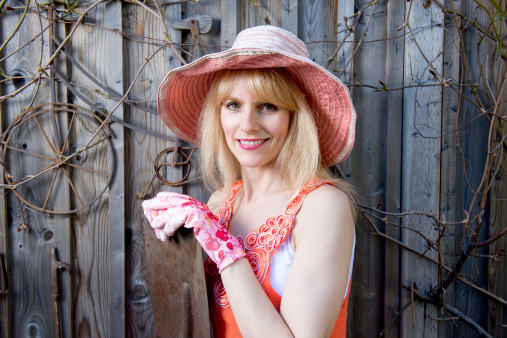 Attractive woman with gardening hat and gloves poses in front of old fence