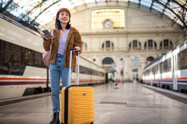 istock A young beautiful Chinese woman is using a mobile phone at a train station while waiting to enter a train car, checking which platform her train is on via a mobile app 1785564801