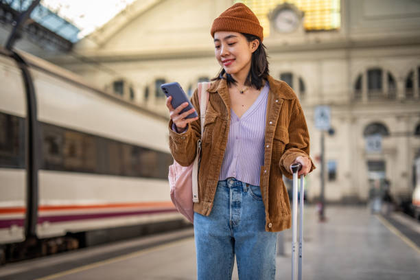 istock A young beautiful Chinese woman is using a mobile phone at a train station while waiting to enter a train car, checking which platform her train is on via a mobile app 1785565330