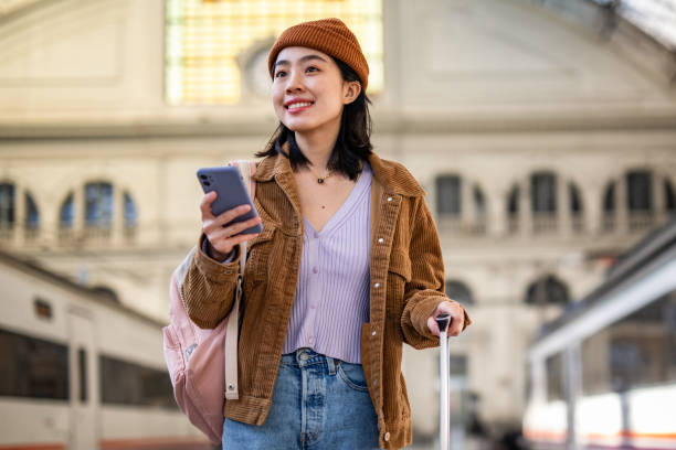 istock A young beautiful Chinese woman is using a mobile phone at a train station while waiting to enter a train car, checking which platform her train is on via a mobile app 1785565338