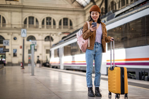 istock A young beautiful Chinese woman is using a mobile phone at a train station while waiting to enter a train car, checking which platform her train is on via a mobile app 1785565356