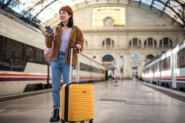 istock A young beautiful Chinese woman is using a mobile phone at a train station while waiting to enter a train car, checking which platform her train is on via a mobile app 1785565365