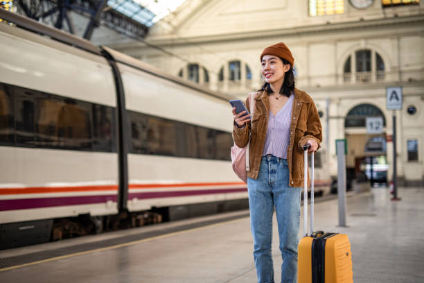 istock A young beautiful Chinese woman is using a mobile phone at a train station while waiting to enter a train car, checking which platform her train is on via a mobile app 1785565470