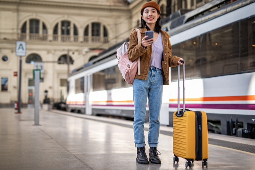 A young beautiful Chinese woman is using a mobile phone at a train station while waiting to enter a train car, checking which platform her train is on via a mobile app